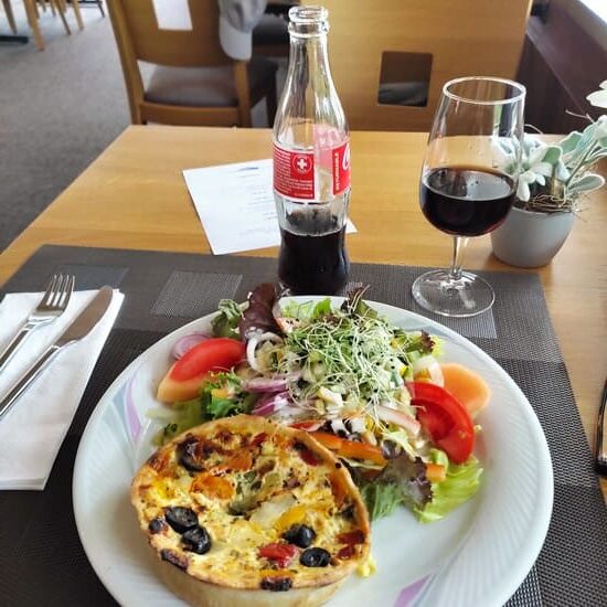 Plate with quiche and salad, soda bottle and glass on wooden table