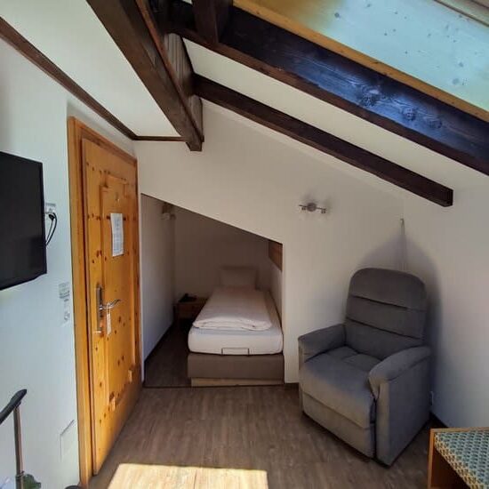 Hotel room with small bed in alcove, chair and skylight