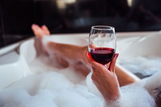 Woman with a glass of wine relaxing in a bubble bath