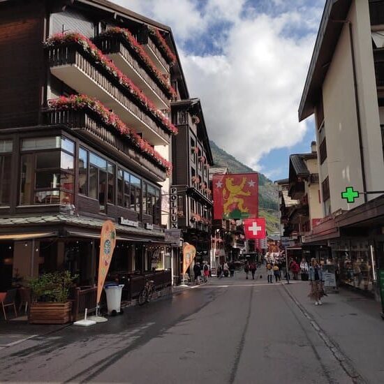 Main street of Zermatt with typical Swiss houses with flowers on balcony and flags hanging over street