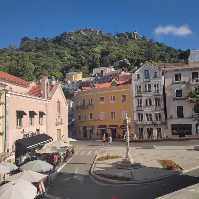 The main square of Sintra's Old Town is surrounded by colorful buildings. In the background, the Moorish Castle can be seen on top of green wooded hills.