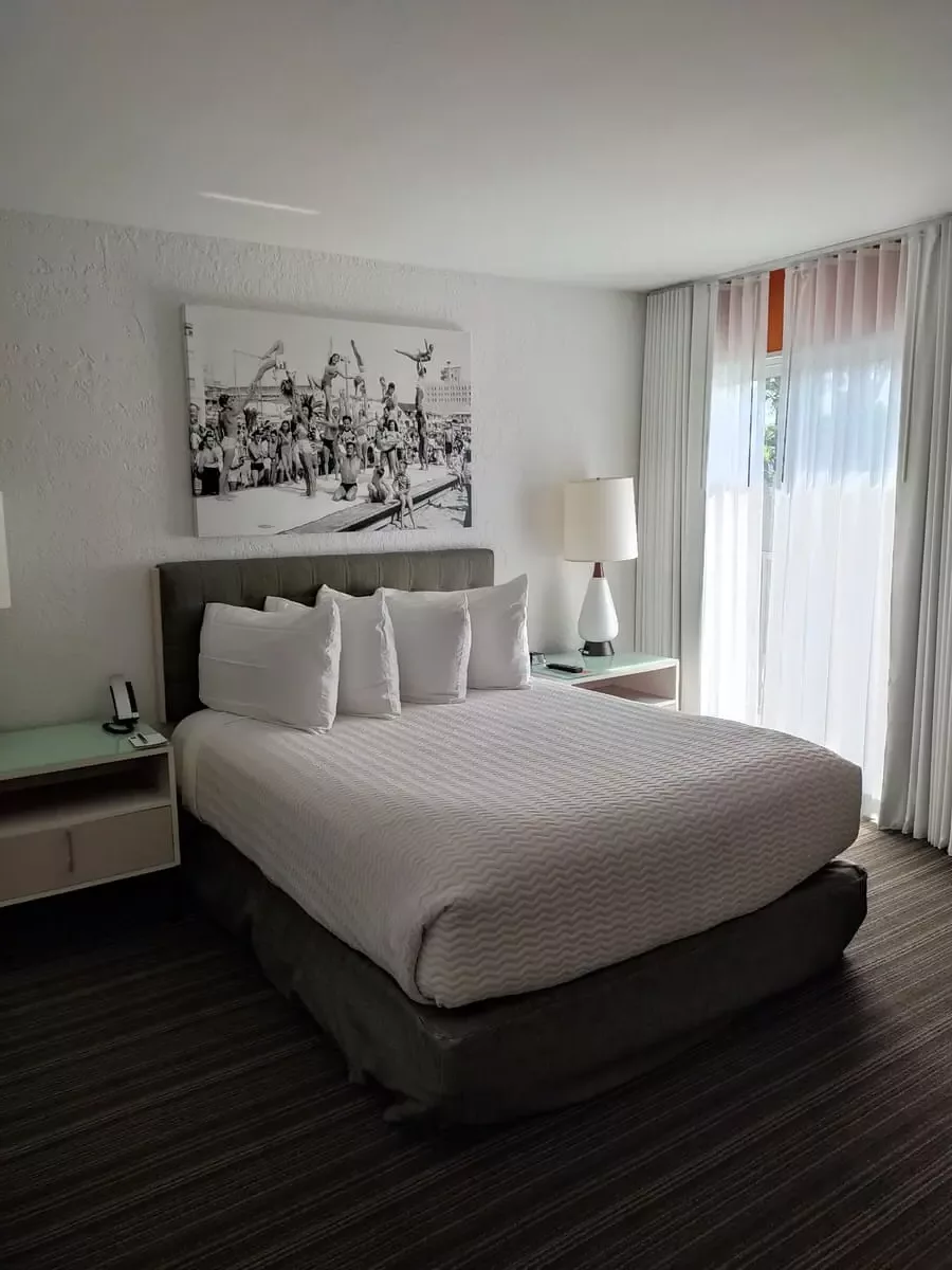 Queen-sized bed in white and black under a large white and black picture. On the left is a glass balcony door.