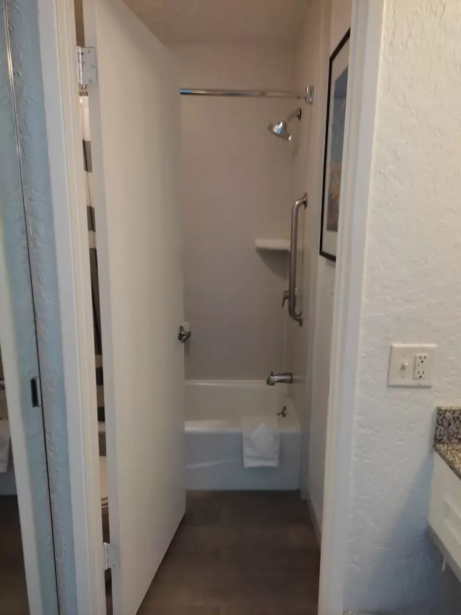 View of small bathroom at Inn at Venice Beach through doorway. There is a toilet behind the door and a low bathtub.