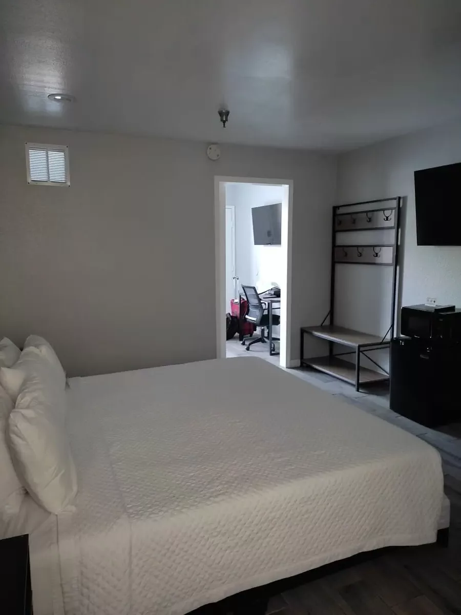 Large bed with white cover at Capri Suites Anaheim. Across the room a door leads in the front room. On the wall is a fridge, microwave, and a small coatrack