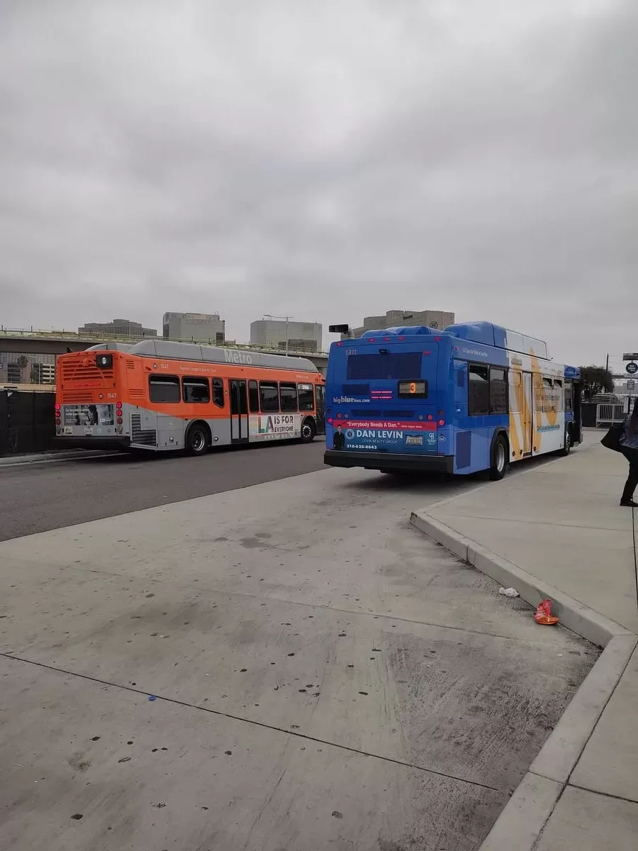 An orange LA Metro bus and a blue Santa Monica Big Blue Bus at the Bus Center near LAX.