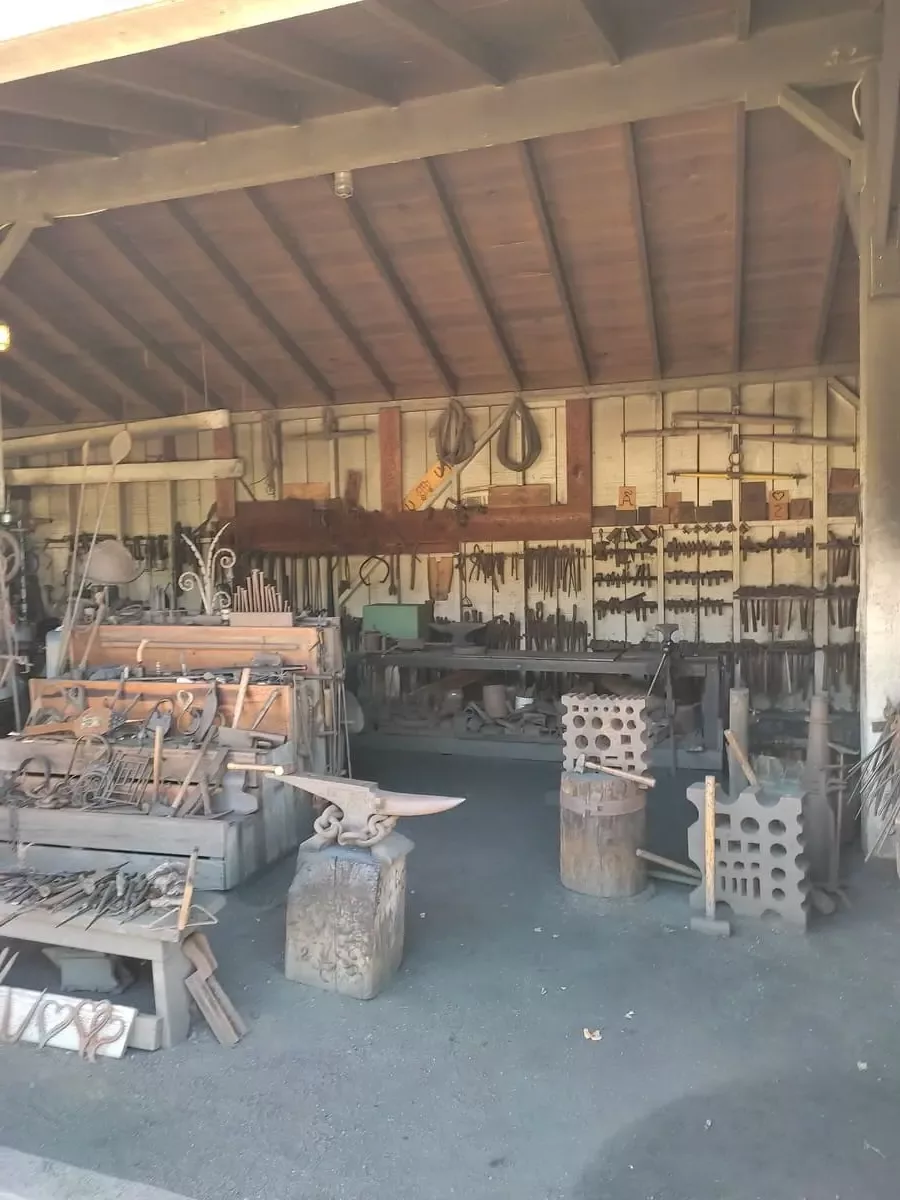 Inside this large shed you see a large number of blacksmithing tools hanging on the walls and displayed on a shelf