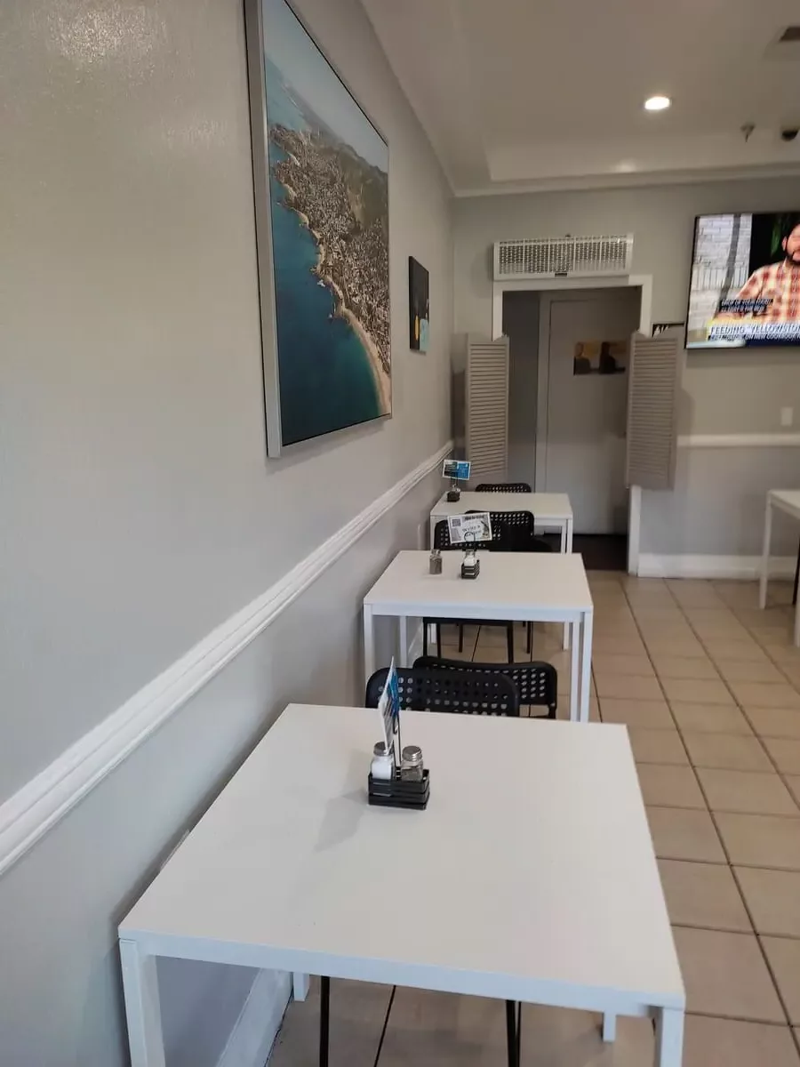 The breakfast room at Capri Suites Anaheim has tan tiles and small white tables with black chairs.