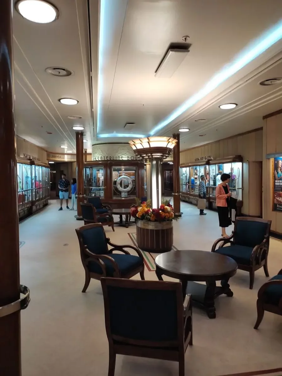 Upscale lounge area with tables and chairs on Promenade Deck surrounded by shop windows.
