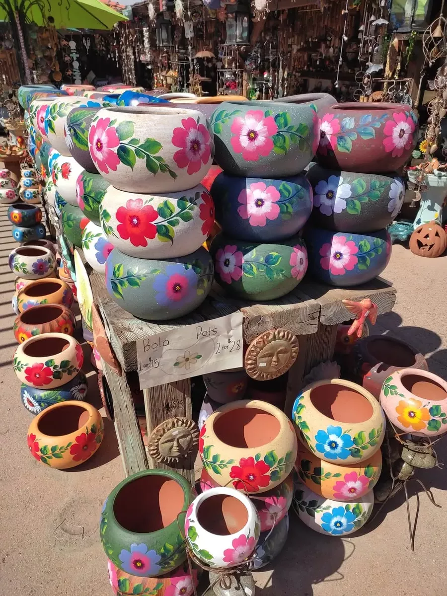 Outside display of various Mexican souvenirs. In the foreground are large flowerpots with colorful flowers painted on them.