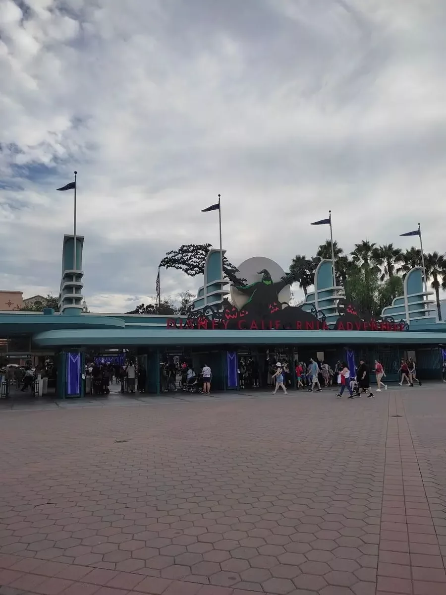 Entrance to Disney California Adventure Park seen from wide plaza. The blue and teal colored entrance is decorated with a large black ghost for Halloween.
