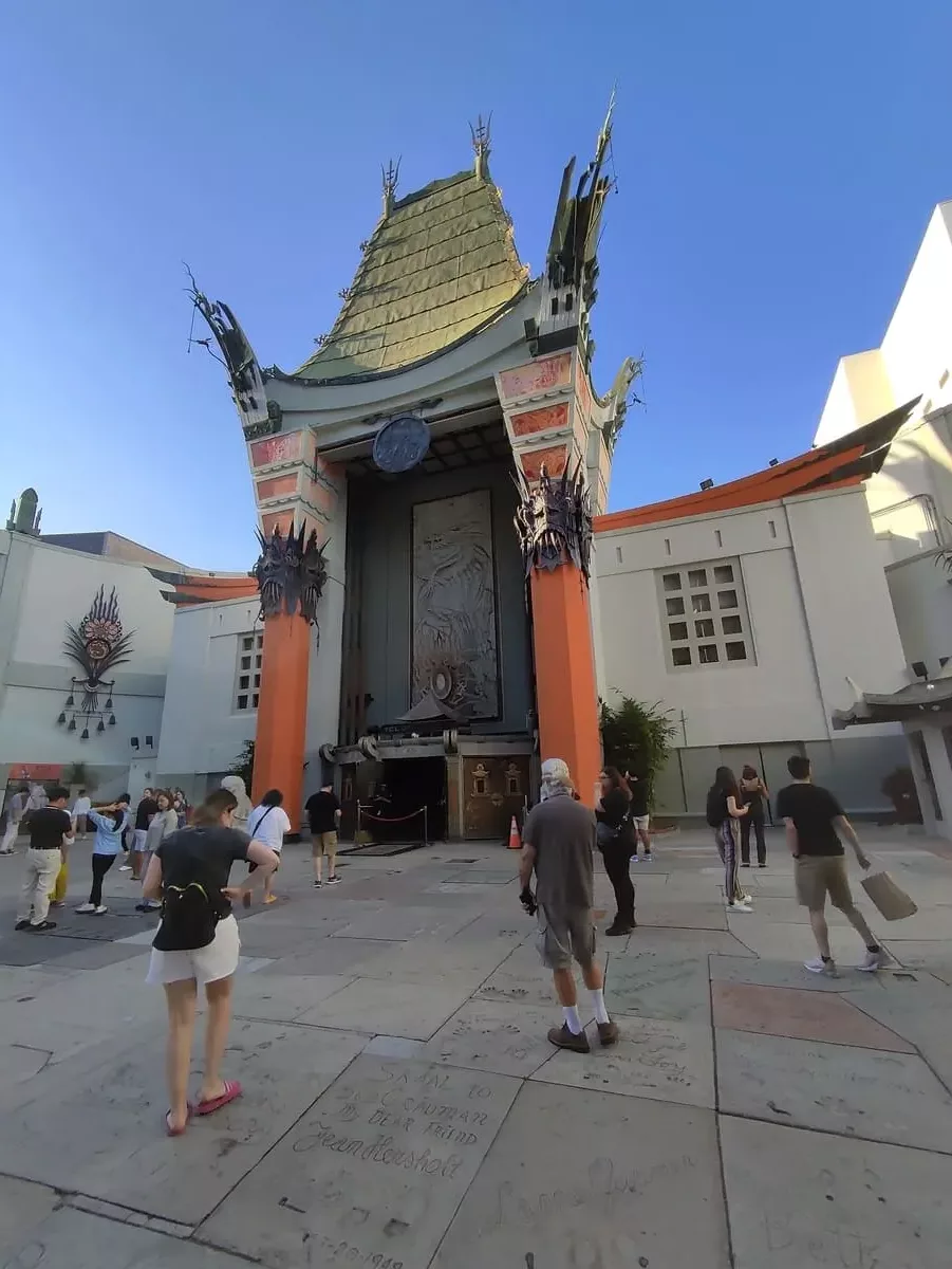 Famous Grauman's Chinese Theater in Pagoda Style in Hollywood. In front of it tourists are looking at hand and foot prints of famous people on the ground.