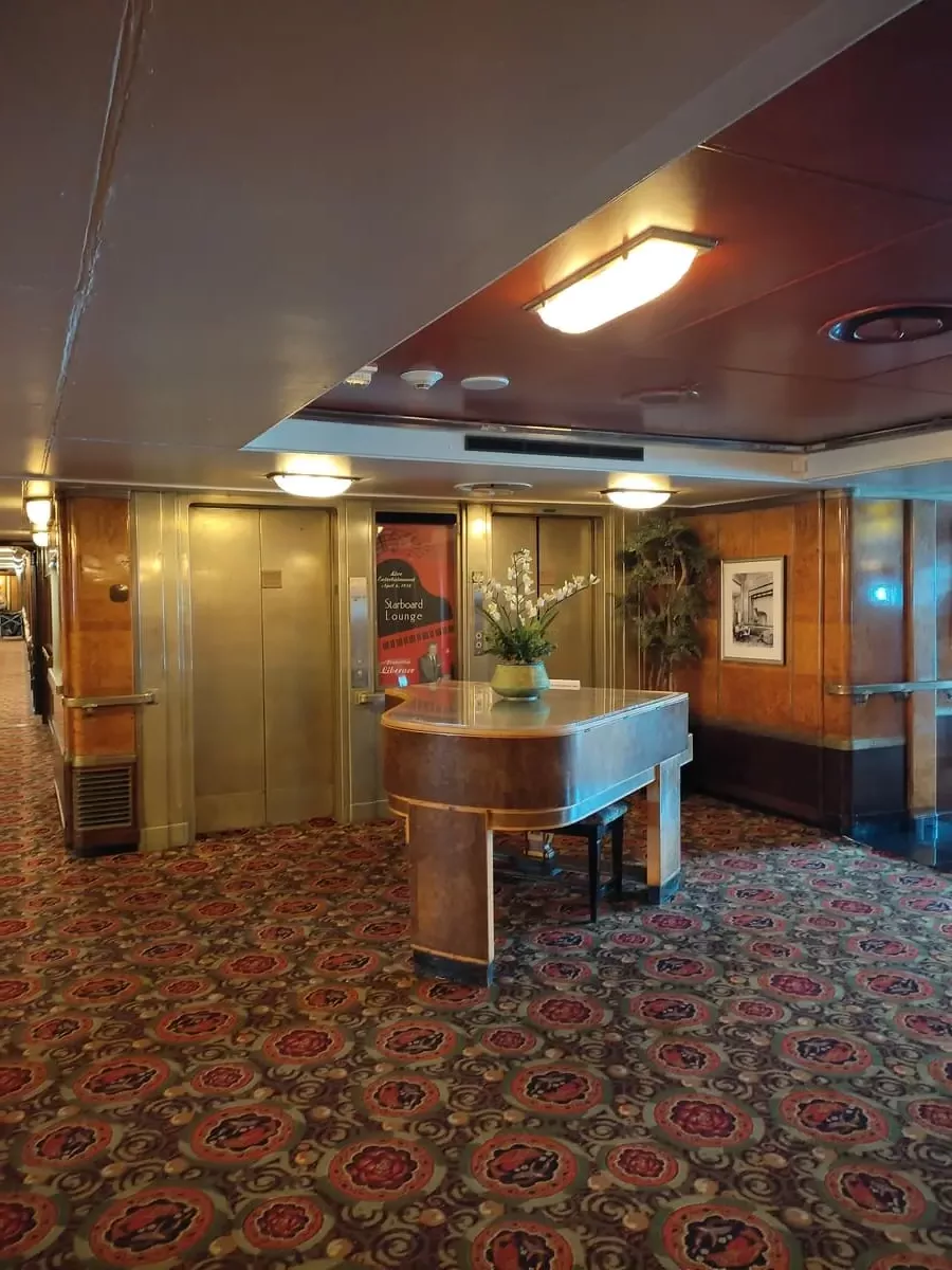 A large piano with flowers on top stands in front of two metal elevator doors.