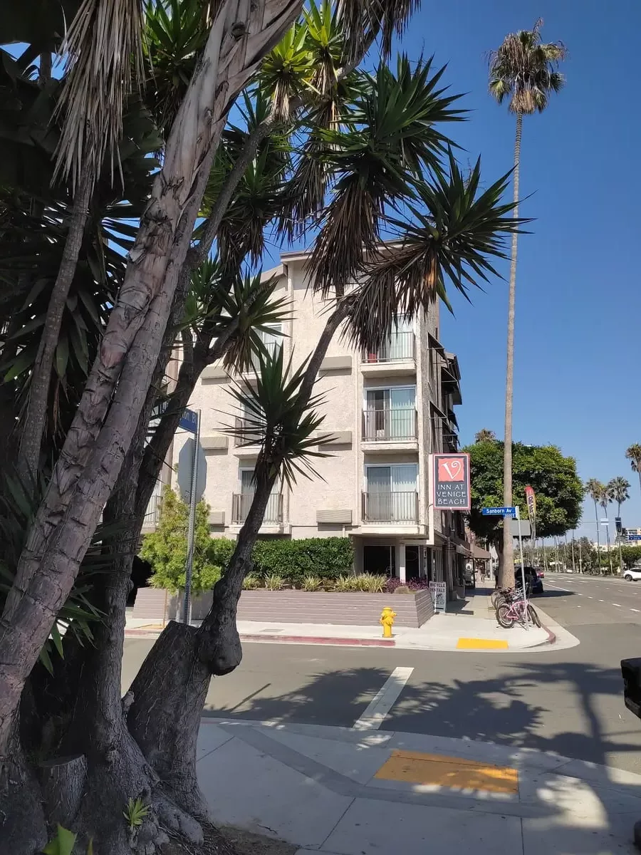 The Inn at Venice Beach resembles a regular apartment building with small balconies. The street is lined by tall palm trees.