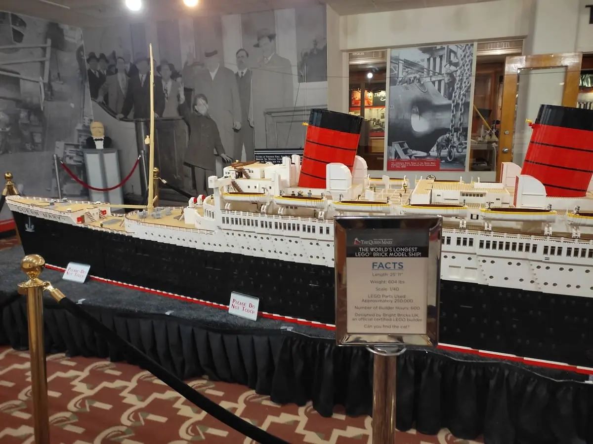 In front of a large Lego model of Queen Mary is a sign with facts about the model