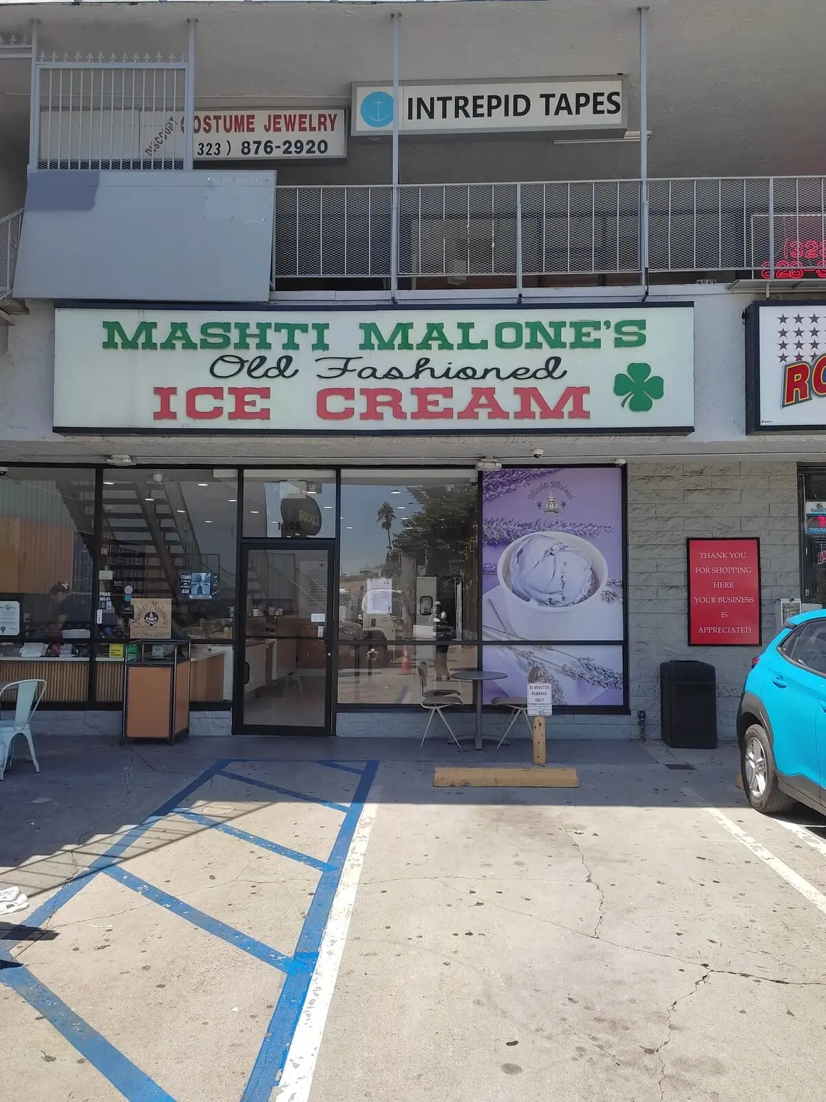 Entrance to Mashti Malone's Old-fashioned ice cream at a strip mall. There are a couple of tables with chairs outside, next to the parking lot
