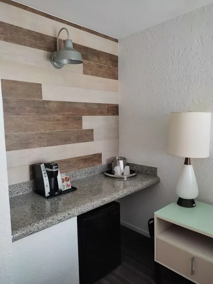 Long marble counter at bedroom wall with coffee machine and small fridge. Next to it nightstand and lamp in Mid-Century style.