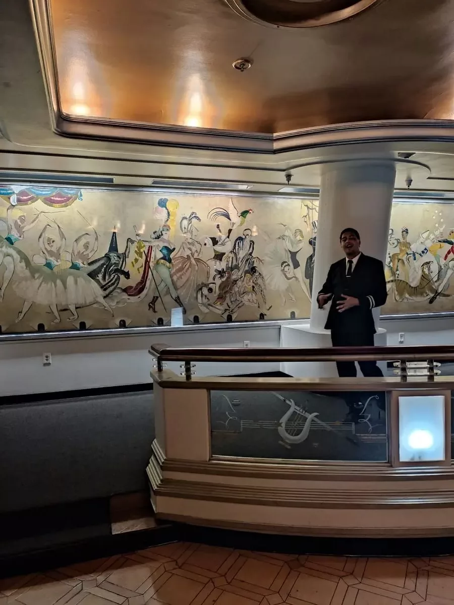 Tour guide telling ghost stories in Queen Mary's former exclusive nightclub. The main features of the room are a large mural of a Venetian party and a balustrade with beautiful glass etchings.