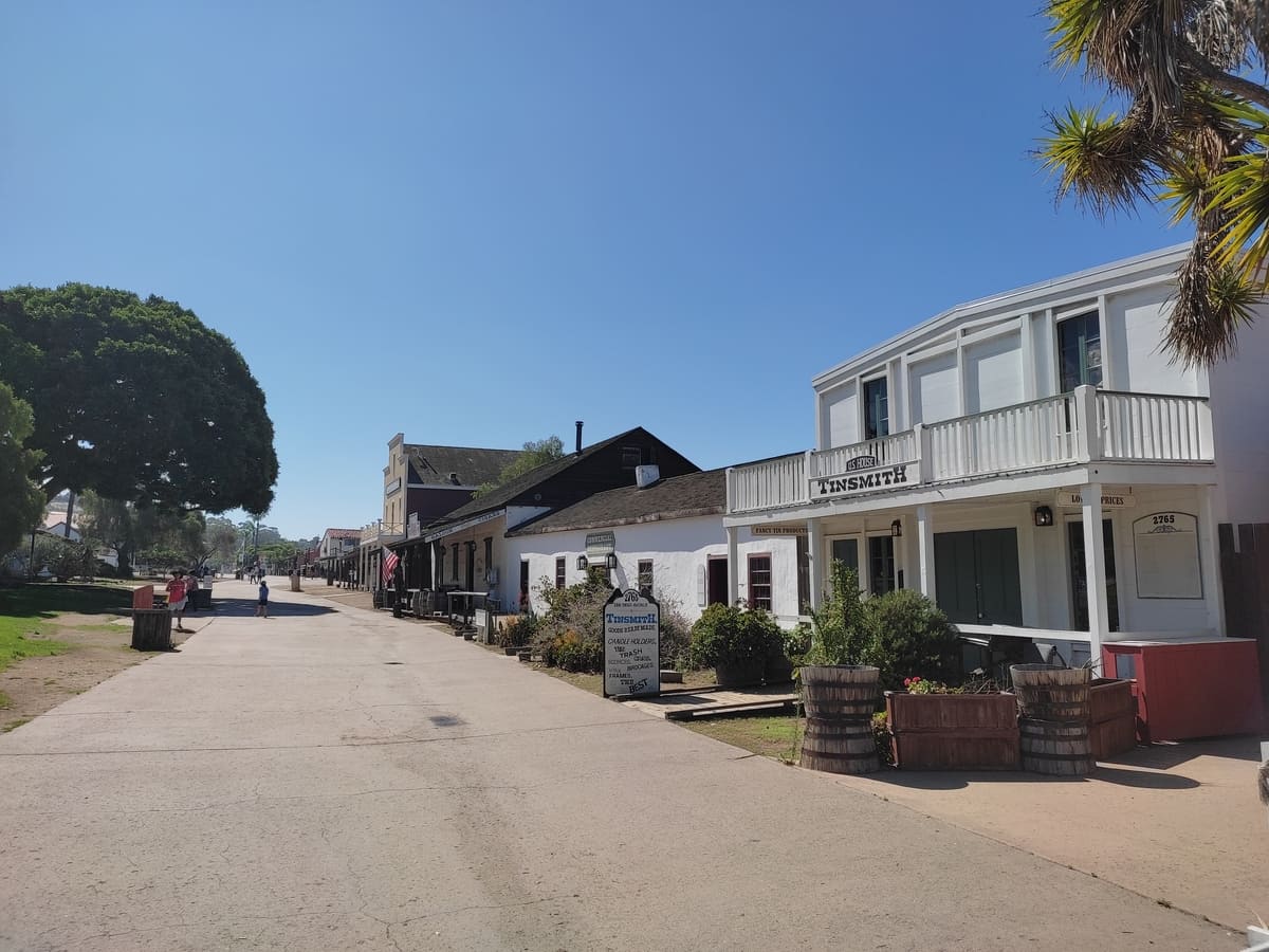 Wide pedestrian street with grass area to the left and low rise old buildings to the right. In these houses you will find quirky shops and small museums.