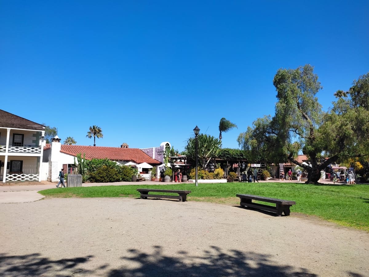 The central grassy area of the state park sports benches and a large tree. It is surrounded by the Mexican-style buildings of Old Town.