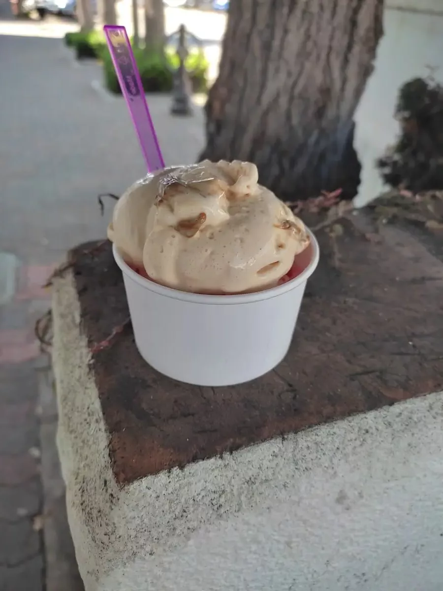 Small tub with ice cream on a stone wall. The top caramel ice-cream has caramel pieces swirled in but is partly melted