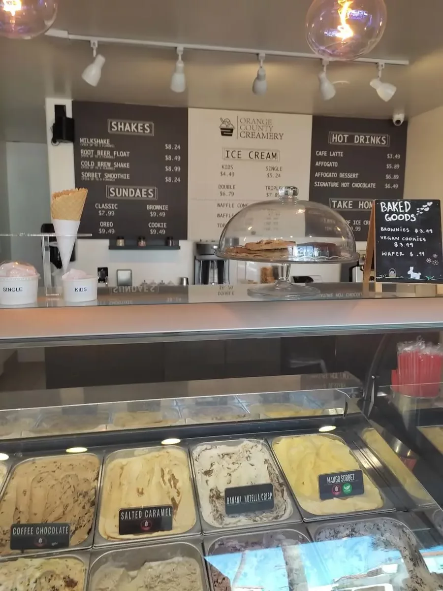 Inside of ice cream shop with menu on back wall and containers with different flavors under a glass cover up front