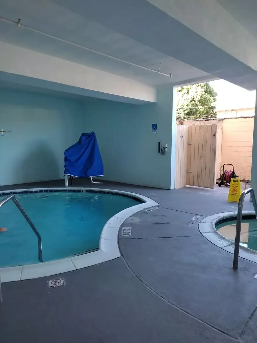Small hot tub and fairly small pool in a covered area with grey cement flooring at Capri Suites Anaheim