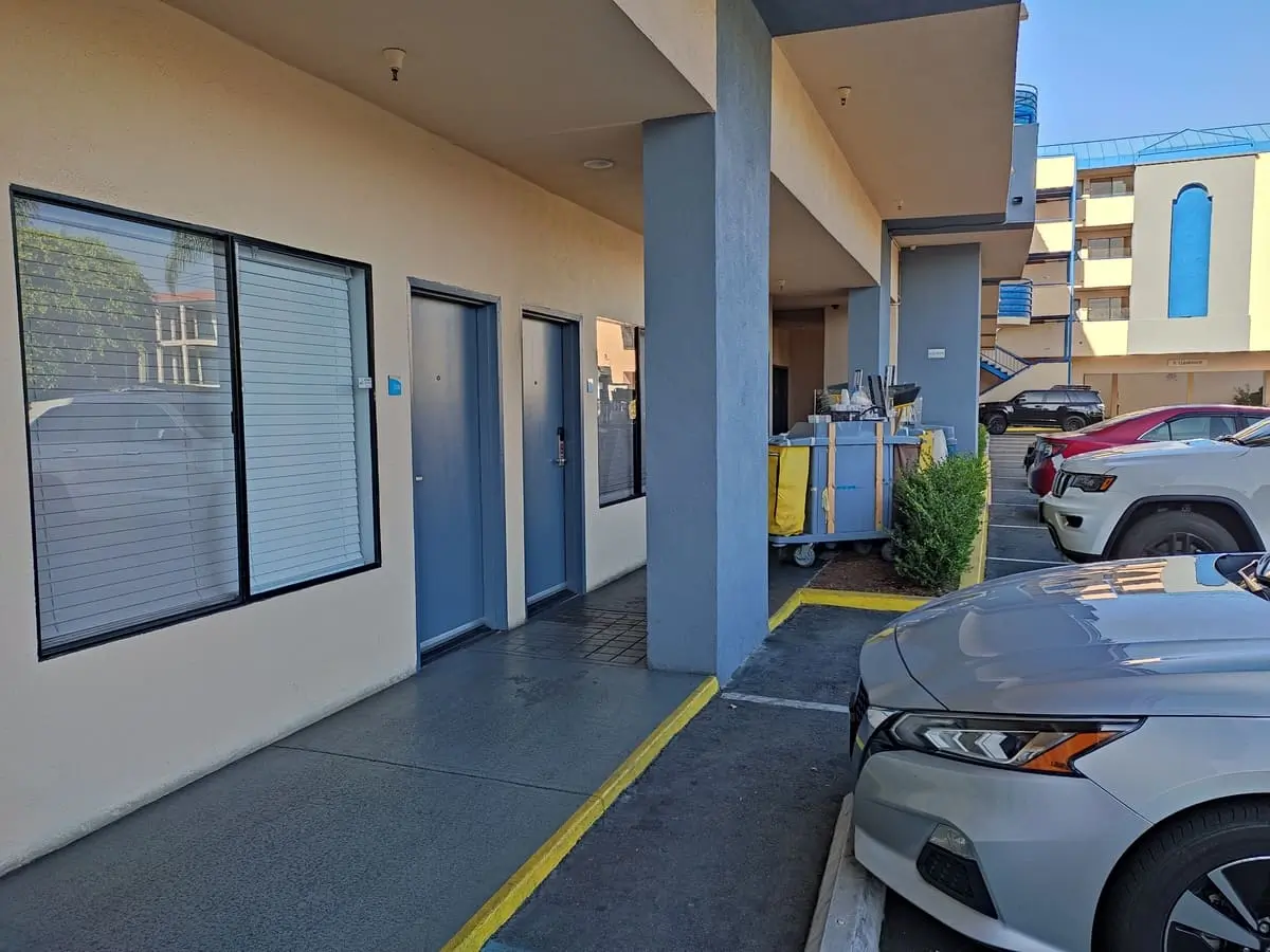 Motel-style Capri Suites in Anaheim with cars parked next to rooms. There area large windows and blue doors leading to the rooms.