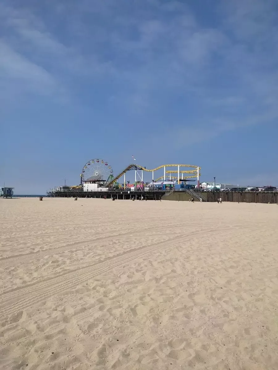 White swath of sand at Santa Monica Beach. In the distance is Santa Monica pier with ferris wheel and roller coaster.