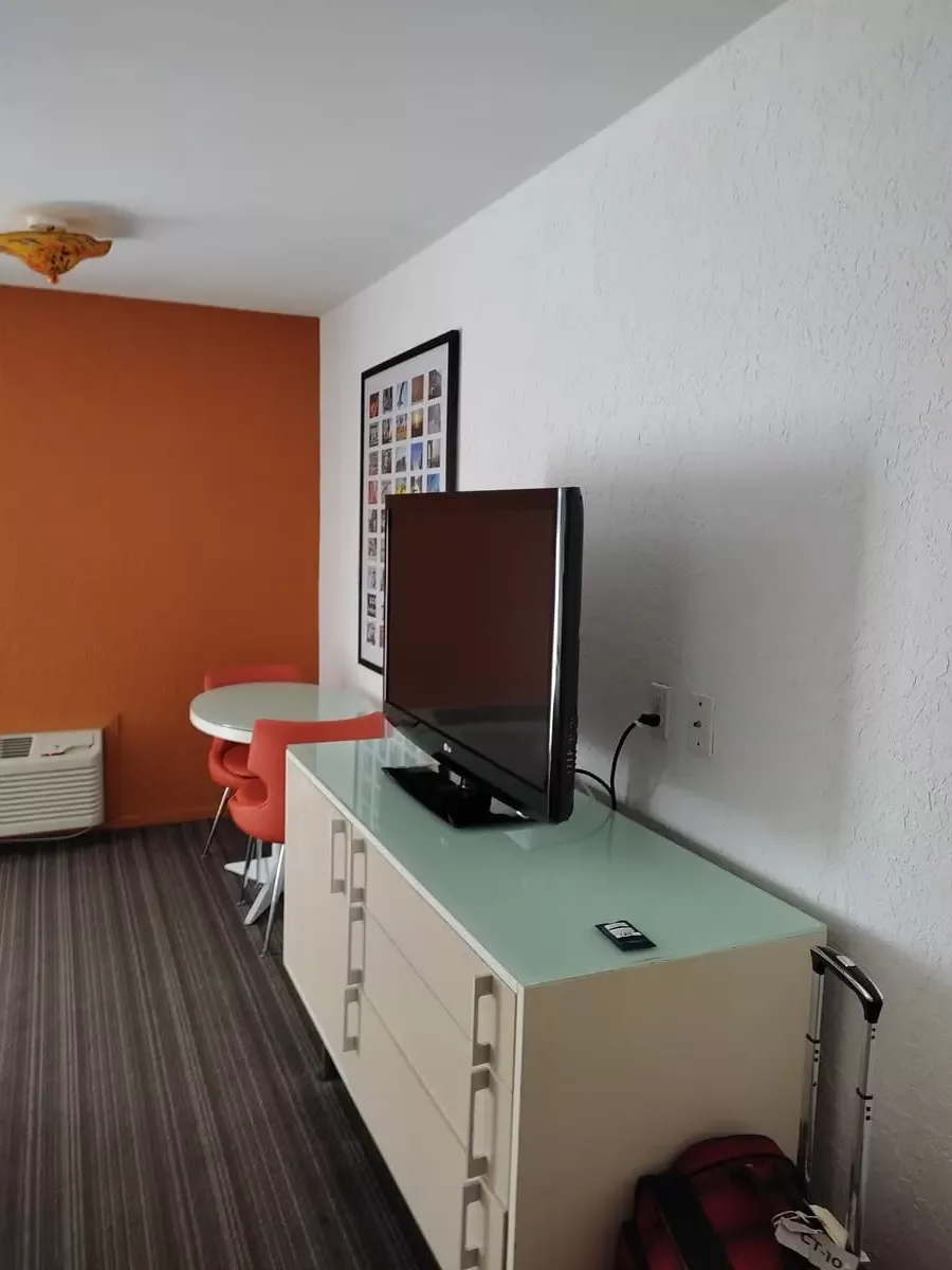 Cool mid-century decor at Inn at Venice Beach: Orange wall, round table with two orange chairs, cabinet with TV and pale green top