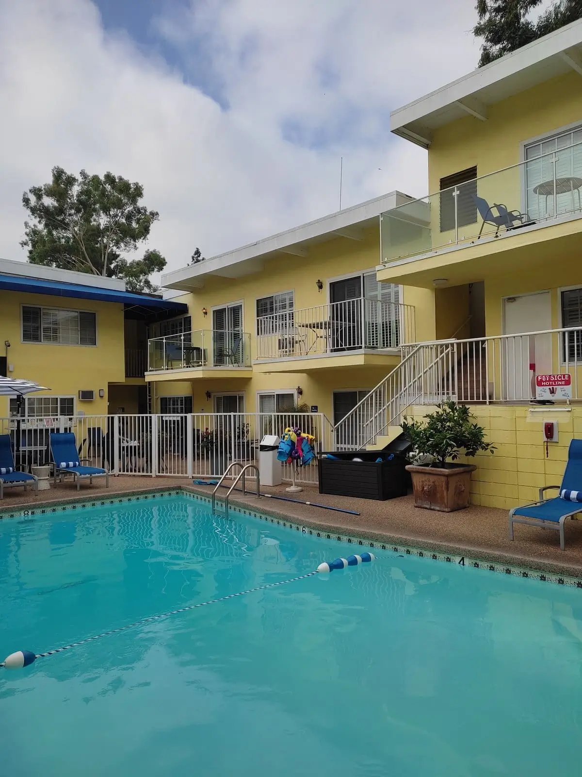 Small pool with sun loungers in courtyard of Magic Castle Hotel. The surrounding low-level apartment building is a bright yellow.