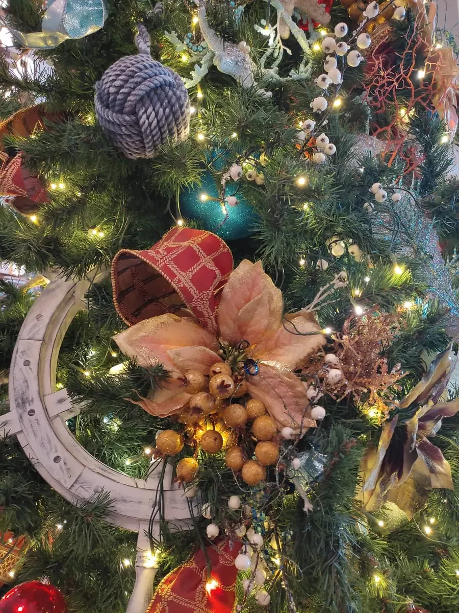 Close-up of Christmas tree decorations with colors mainly red, grey, and peach. There is a large ship's wheel, mistletoe berres, and a ball of rope.