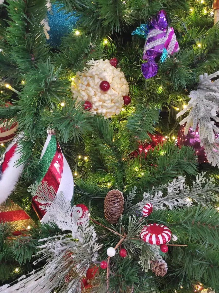 Close-up of Christmas tree decorations with colors mainly red and white. There is a large popcorn ball, a pine cone, and candy.