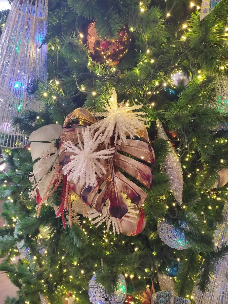 Close-up of Christmas tree decorations with colors mainly blue, white, and metallic bronze. There is a big metal leaf and various ornaments.