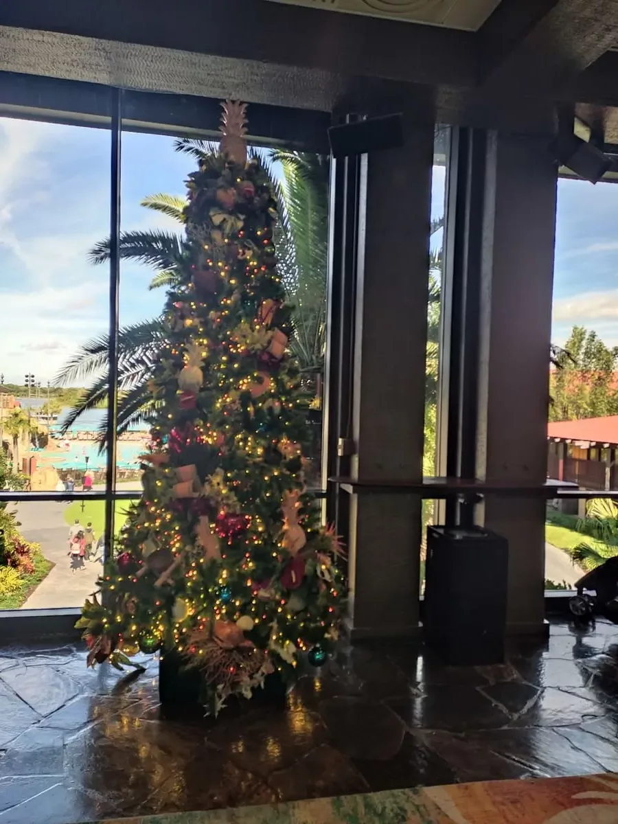 Southsea-themed Christmas Tree at Polynesian Resort in front of large window with view of gardens and pool