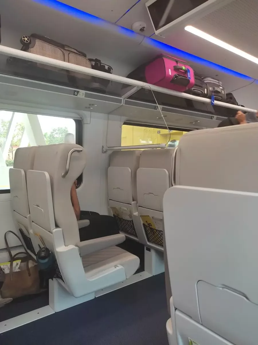 Train interior with modern pale grey seats and luggage rack overhead