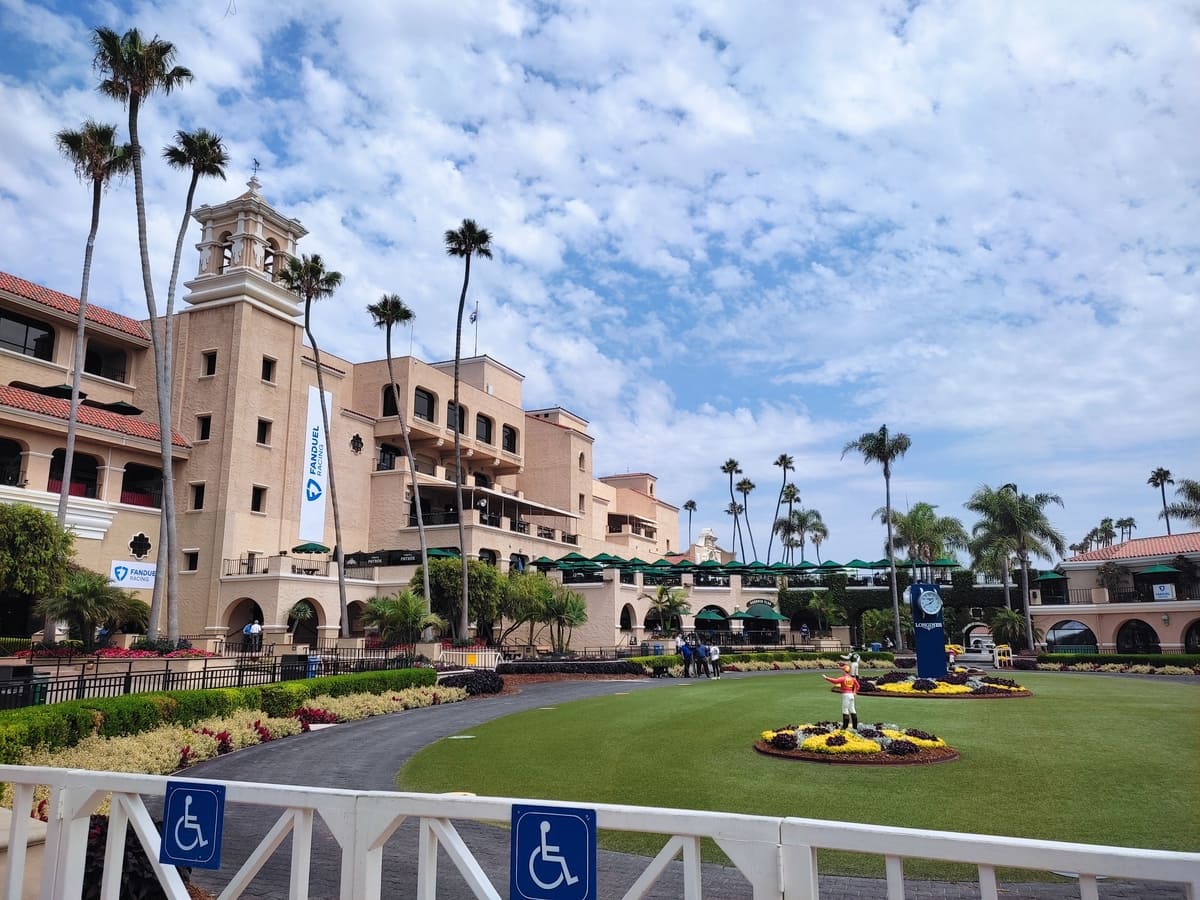 The distinctive pink Spanish style main building of Del Mar's race track sits right next to the green oval of the winner's circle where horses and riders come to collect their prize