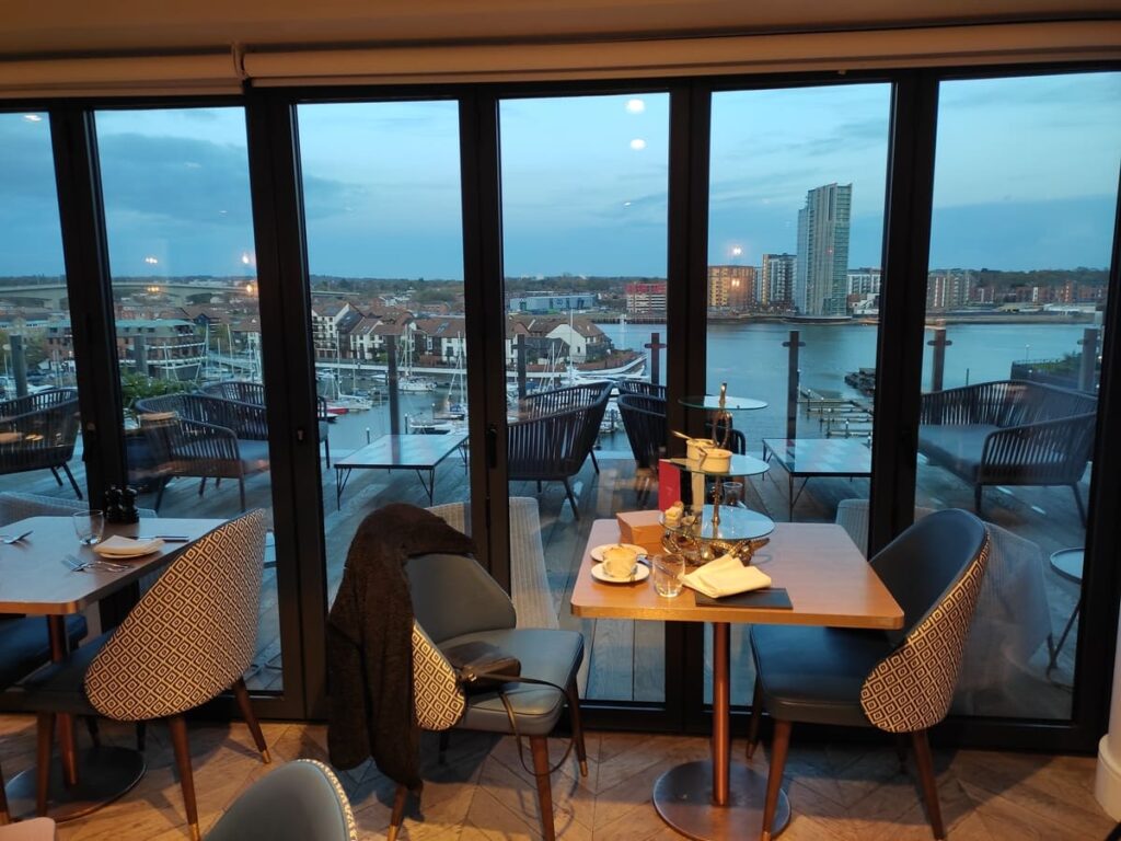 Small restaurant table in front of large glass windows with view of harbour