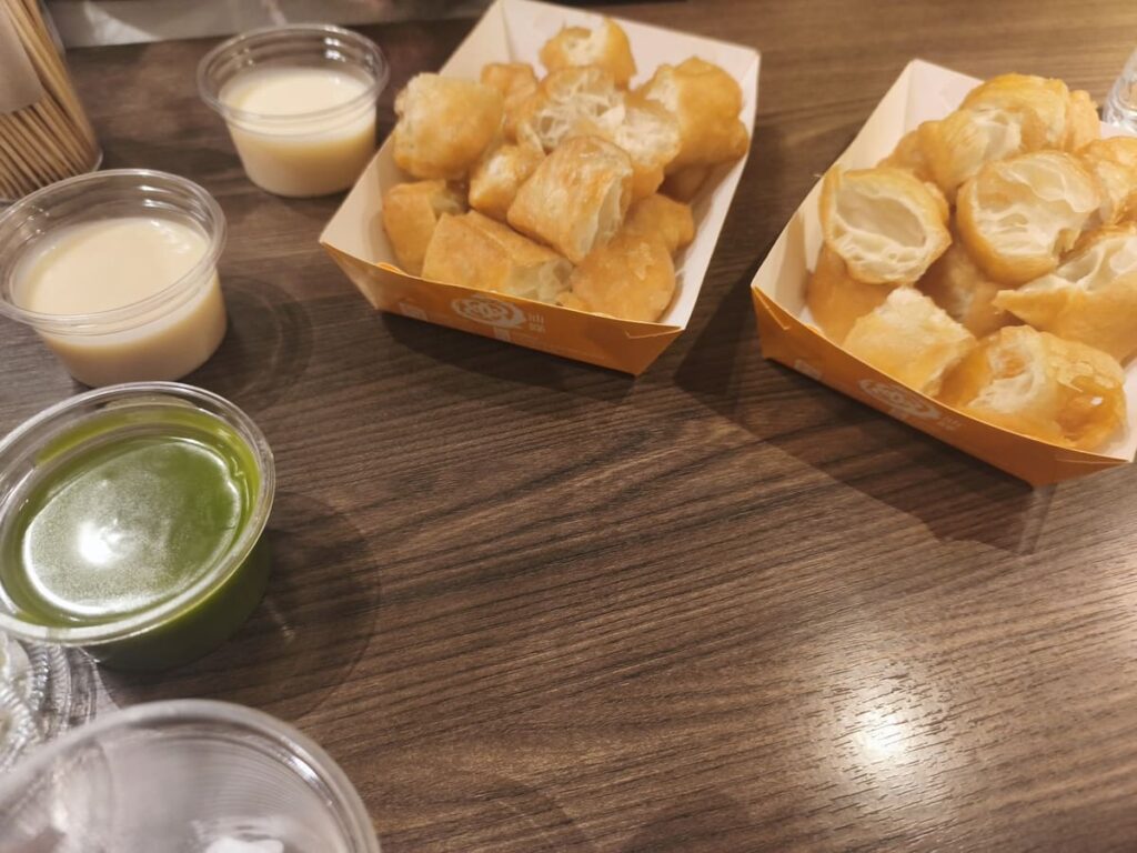Fried dough pieces and small containeres with condensed milk and pandan custard