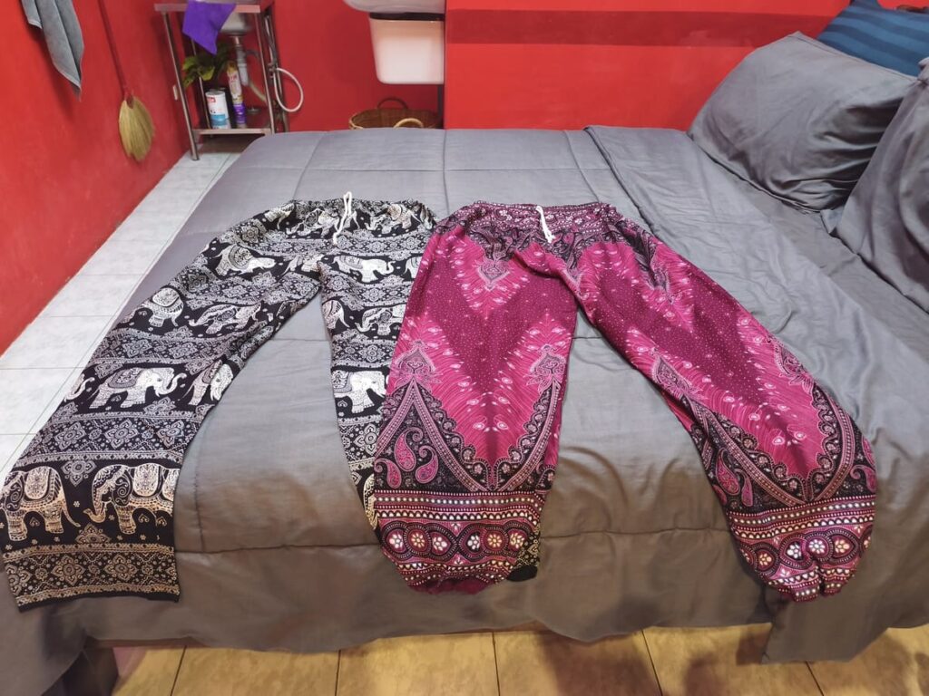 Two pairs of elephant pants (one black and white, the other pink, black, and white) on a bed