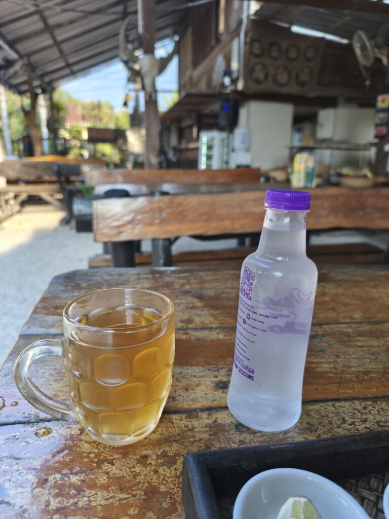 Glass mug with ginger drink and small bottle of water on wooden table