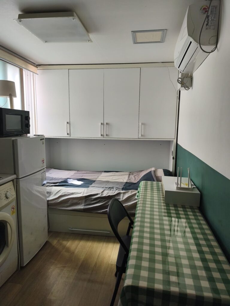 Narrow room with table, bed and kitchenette