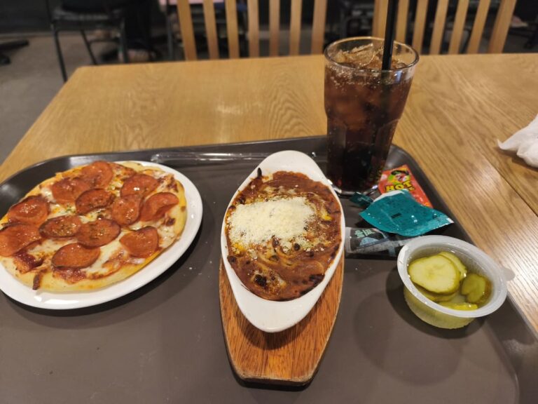Table with small pizza, soda, pickles, small spaghetti dish