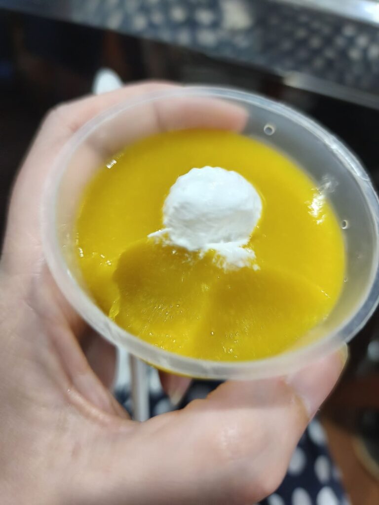 Hand holding small container with mango custard